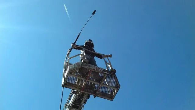 Dušan Holub na pracovní plošině s tlakovou tryskou proti modré obloze